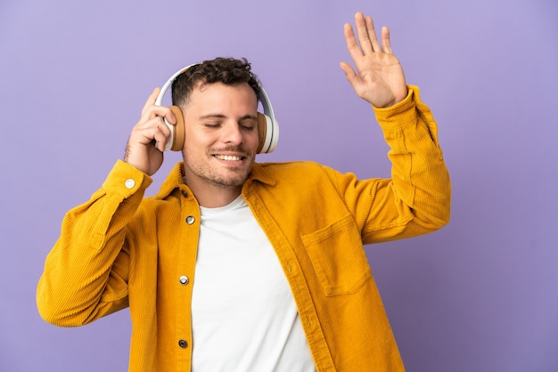 Jeune bel homme caucasien isolé sur violet écoute de la musique et de la danse