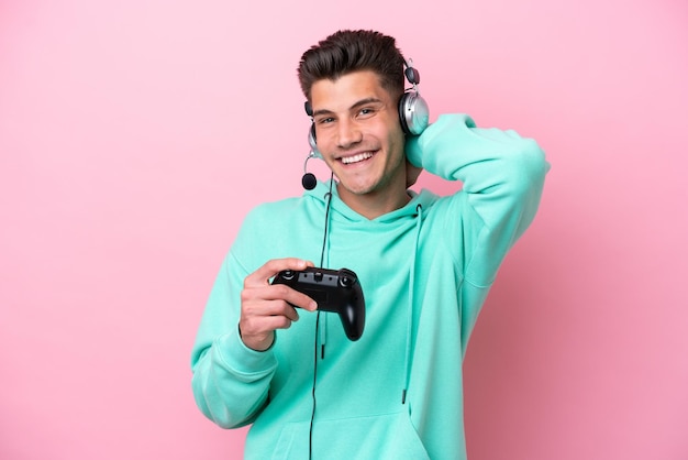 Jeune bel homme caucasien jouant avec un contrôleur de jeu vidéo isolé sur fond rose en riant