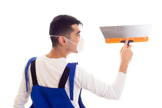 Jeune bel homme en chemise blanche et combinaison bleue avec un respirateur blanc sur son visage à l'aide d'une spatule