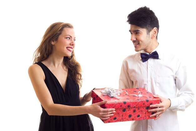 Jeune bel homme en chemise blanche avec noeud papillon noir et belle jeune femme tenant un cadeau rouge
