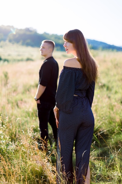 Jeune bel homme en chemise noire et pantalon en attente de sa jolie femme, debout dans un champ au coucher du soleil d'été