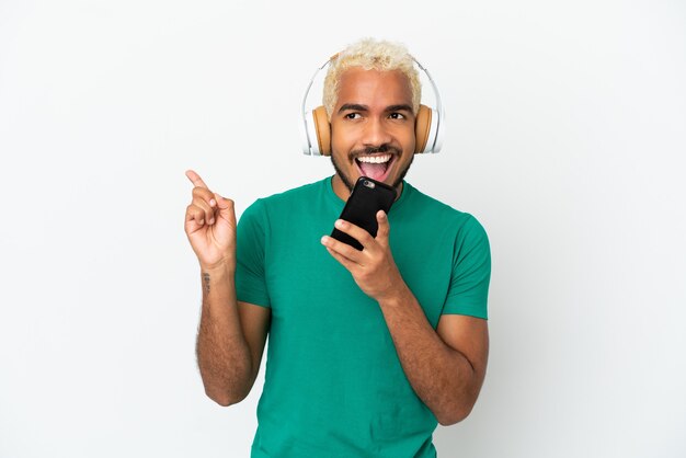 Jeune bel homme colombien isolé sur fond blanc, écouter de la musique avec un mobile et chanter