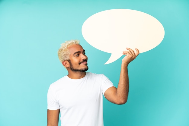 Photo jeune bel homme colombien isolé sur fond bleu tenant une bulle de dialogue vide