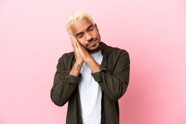 Jeune bel homme colombien isolé sur fond rose faisant un geste de sommeil dans une expression adorable