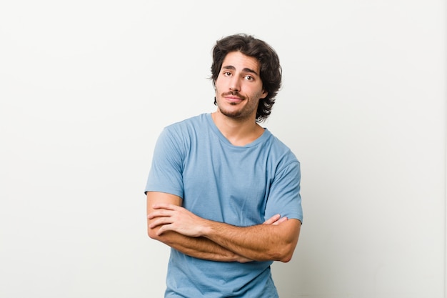 Jeune bel homme contre un mur blanc malheureux à la recherche à huis clos avec une expression sarcastique.