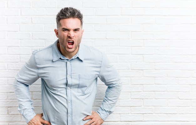 Jeune bel homme contre un mur de briques criant très en colère et agressif.