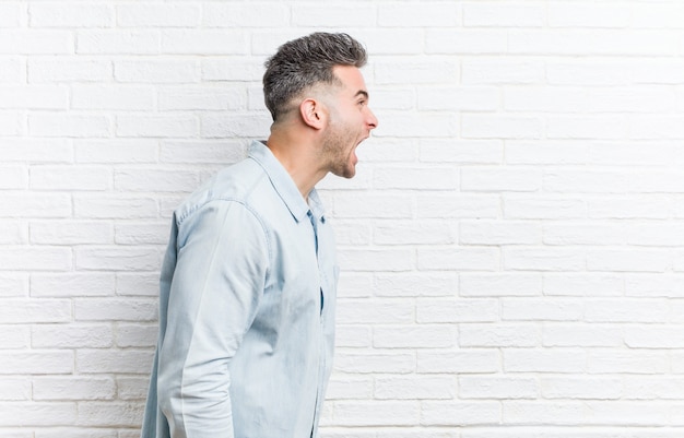 Jeune bel homme contre un mur de briques criant vers un espace de copie