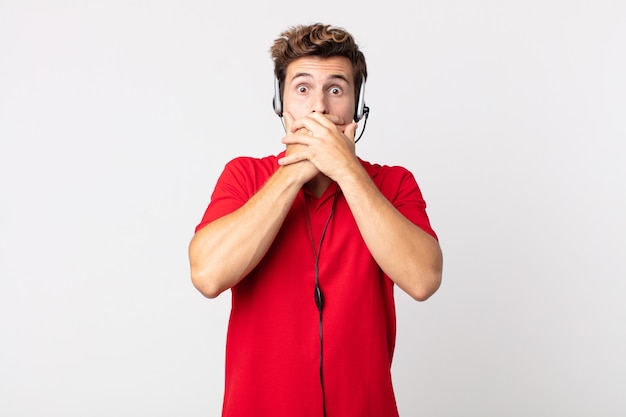 Jeune bel homme couvrant la bouche avec les mains avec un choc. concept de télévendeur