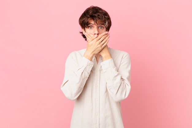 Jeune bel homme couvrant la bouche avec les mains avec un choqué