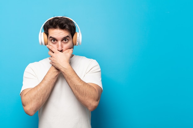 Jeune bel homme couvrant la bouche avec les mains avec une expression choquée et surprise, gardant un secret ou disant oups