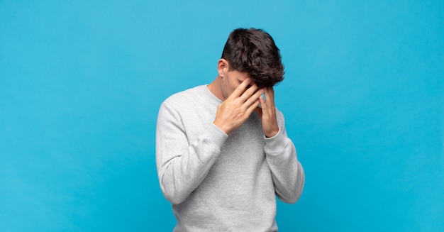 Jeune bel homme couvrant les yeux avec les mains avec un triste