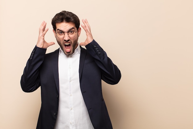 Jeune bel homme criant avec les mains en l'air, se sentant furieux, frustré, stressé et bouleversé