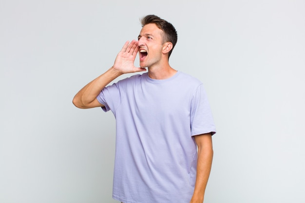 Jeune bel homme crier fort et en colère pour copier l'espace sur le côté, avec la main à côté de la bouche