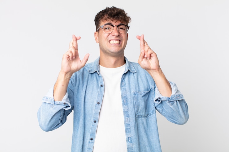 Photo jeune bel homme croisant les doigts avec anxiété et espérant bonne chance avec un regard inquiet