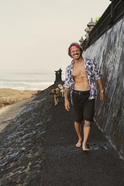 Un jeune bel homme dans un bandana rouge se promène le long de l'océan à la plage.