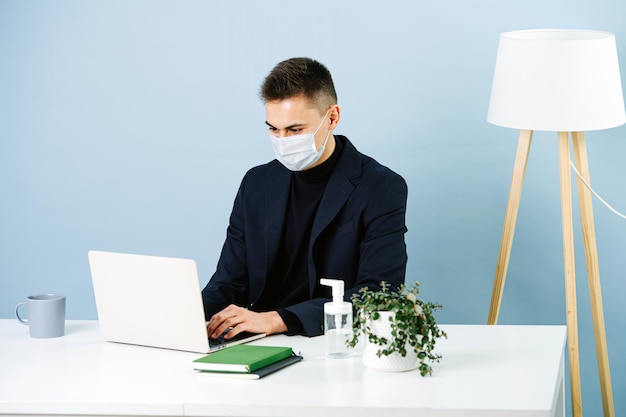 Jeune bel homme dans un masque médical travaillant derrière le bureau