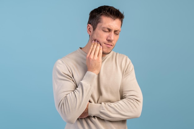 Jeune bel homme debout sur fond bleu isolé touchant la bouche avec la main avec une expression douloureuse à cause d'un mal de dents ou d'une maladie dentaire sur les dents