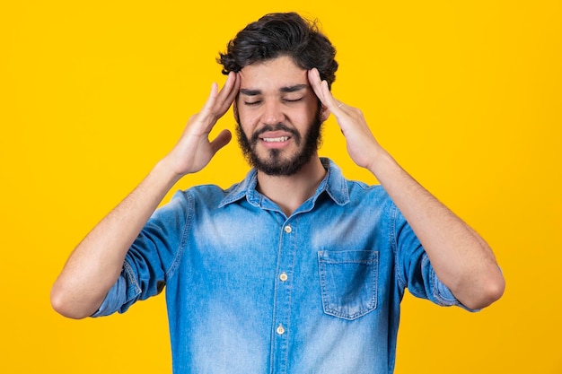 Jeune bel homme debout sur fond jaune isolé souffrant de maux de tête désespérés et stressés parce que la douleur et la migraine Mains sur la tête