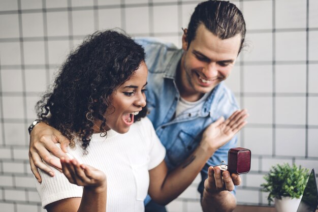 Photo jeune bel homme donnant la bague pour la surprise à sa petite amie et parler ensemble assis dans le salon à la maison