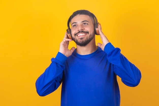 Jeune bel homme écoutant de la musique sur fond de studio jaune casque isolé souriant heureux