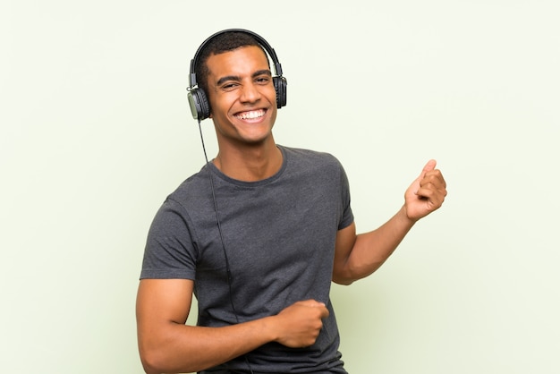 Jeune bel homme écoute de la musique avec un téléphone portable sur un mur vert isolé