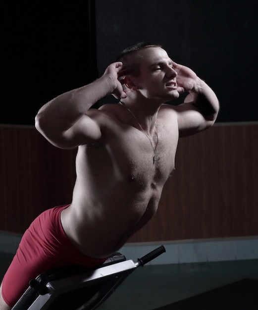 Jeune bel homme effectue des exercices de sport pour renforcer les muscles.photo sur fond noir et a une place pour le texte