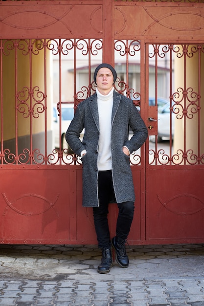 Photo jeune bel homme élégant hipster portant un manteau gris, un pull blanc et un jean noir