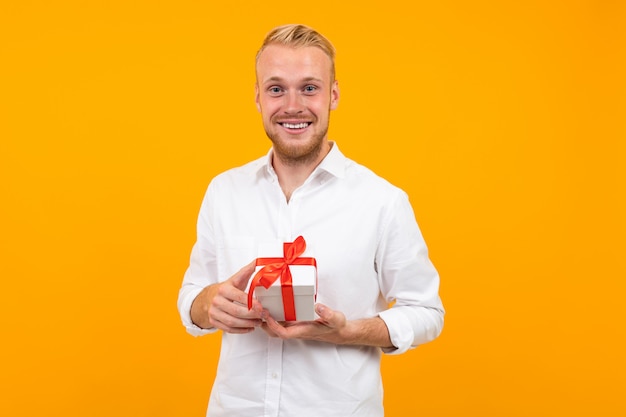 Jeune bel homme est titulaire d'une boîte blanche avec cadeau et sourires isolé sur jaune