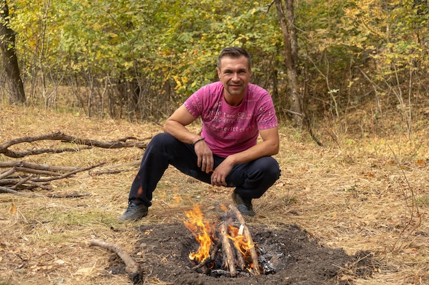 Jeune bel homme fait un feu de camp à l'extérieur dans la forêt d'automne. Feu de joie dans les bois