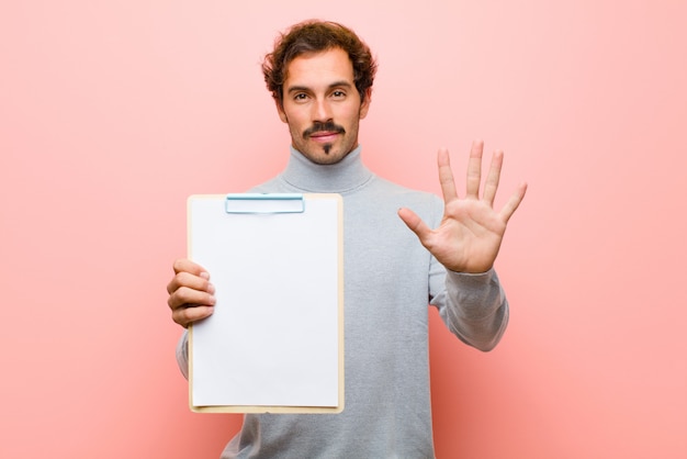 Jeune bel homme avec une feuille de papier contre un mur plat rose