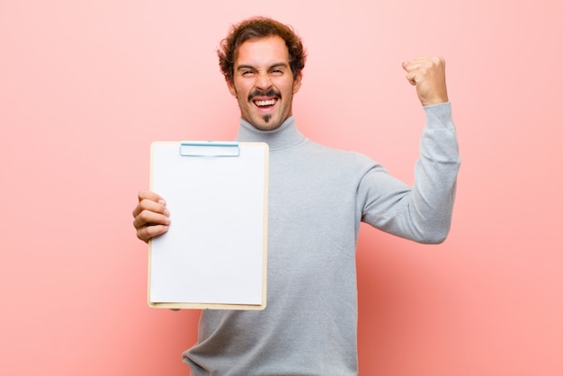 Jeune bel homme avec une feuille de papier mur plat rose