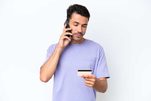 Jeune bel homme sur fond blanc isolé achetant avec le mobile avec une carte de crédit