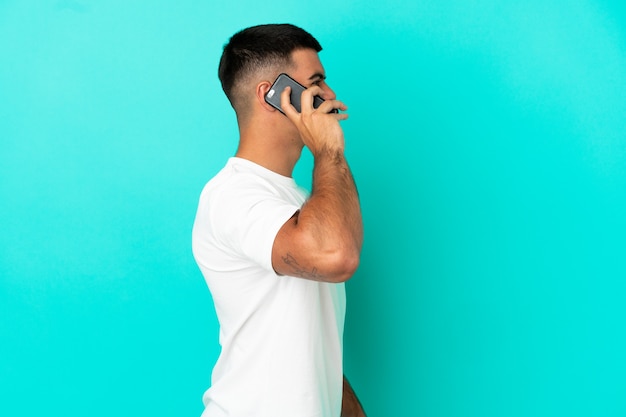 Jeune bel homme sur fond bleu isolé gardant une conversation avec le téléphone portable avec quelqu'un