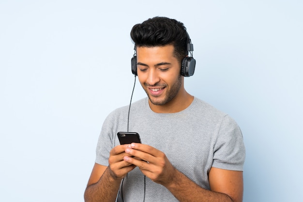 Jeune bel homme sur fond isolé à l'aide du téléphone portable avec un casque