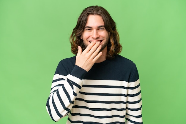 Jeune bel homme sur fond isolé heureux et souriant couvrant la bouche avec la main