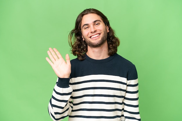 Jeune bel homme sur fond isolé saluant avec la main avec une expression heureuse