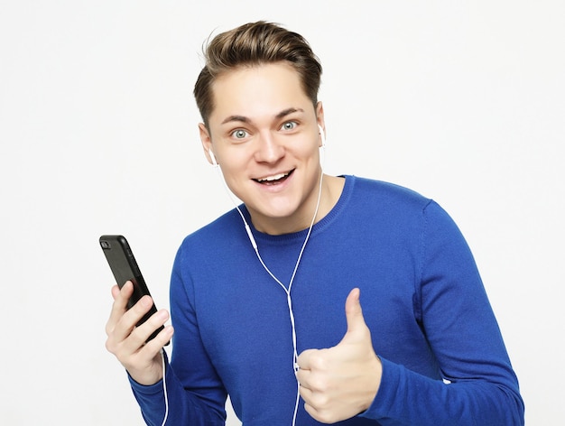 Jeune bel homme sur fond de studio blanc écoutant de la musique sur des écouteurs