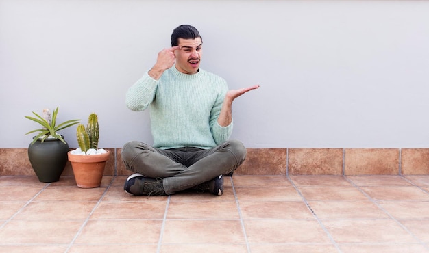 Jeune bel homme gardant et assis sur le sol à l'extérieur