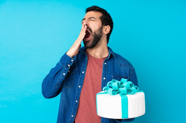 Jeune bel homme avec un gros gâteau sur bleu isolé