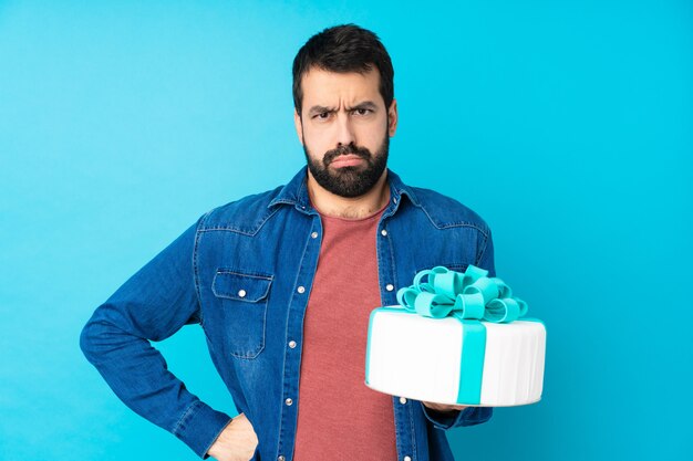 Jeune bel homme avec un gros gâteau sur le mur bleu isolé en colère