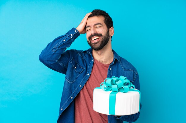 Jeune bel homme avec un gros gâteau sur un mur bleu isolé souriant beaucoup