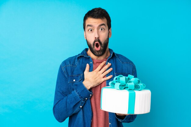 Jeune bel homme avec un gros gâteau surpris et choqué tout en regardant à droite