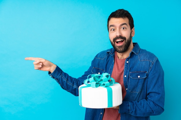 Jeune bel homme avec un gros gâteau surpris et pointant le côté