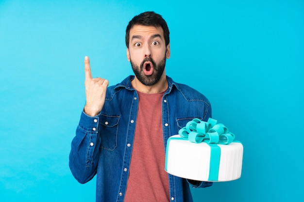 Jeune bel homme avec un gros gâteau surpris et pointant vers le haut