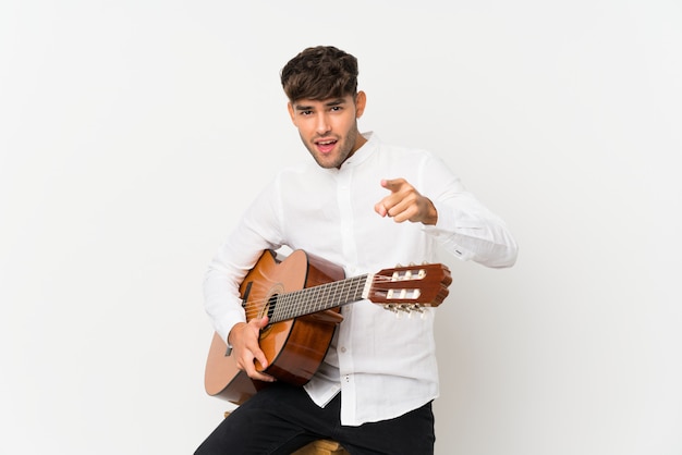 Jeune bel homme avec guitare surpris et pointant devant