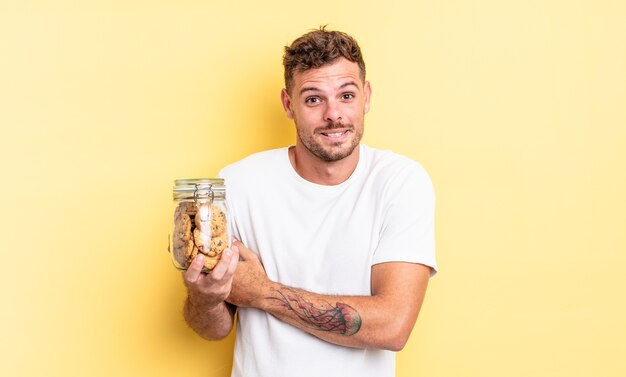 Jeune Bel Homme Haussant Les épaules, Se Sentant Confus Et Incertain Concept De Bouteille De Cookies