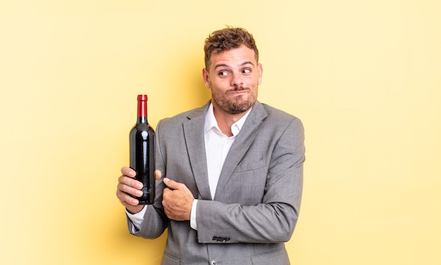 Jeune bel homme haussant les épaules, se sentant confus et incertain. concept de bouteille de vin