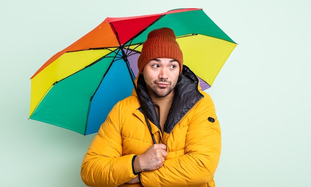 Jeune bel homme haussant les épaules, se sentant confus et incertain. concept de pluie et de parapluie