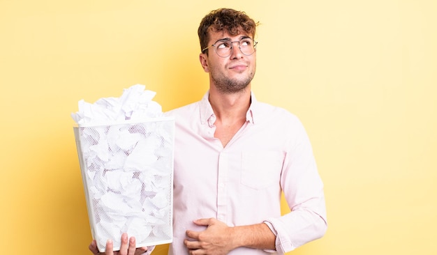 Jeune bel homme haussant les épaules, se sentant confus et incertain. concept de poubelle de boules de papier