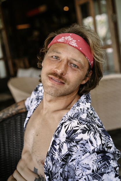 Jeune bel homme hippie dans un bandana rouge, avec un torse nu dans un café à Bali. Heureux homme souriant